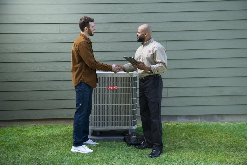 A technician shakes hands with a homeowner in front of a new Bryant AC unit.