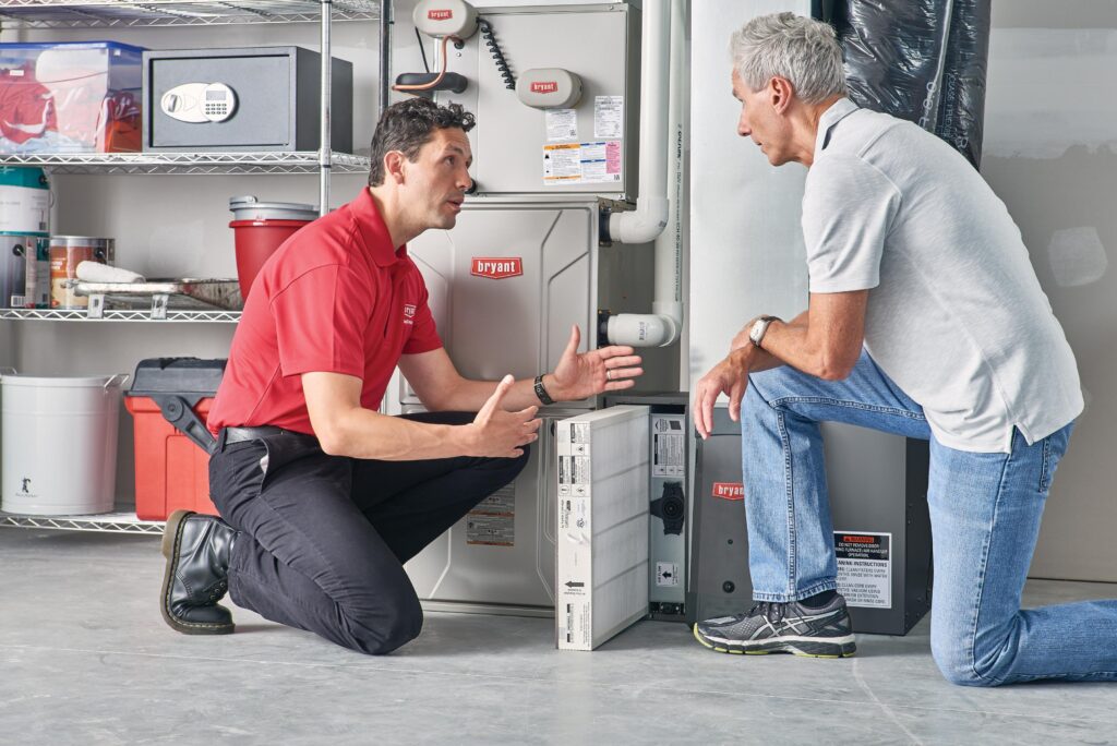 A technician talks with a homeowner while replacing an AC filter, demonstrating how AC units can last longer with maintenance.