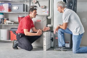 A technician talks with a homeowner while replacing an AC filter, demonstrating how AC units can last longer with maintenance.