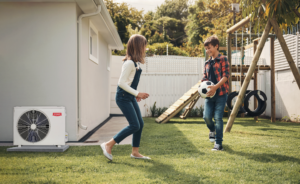 Kids happily playing with a soccer ball outside in their yard with a Bryant air conditioner nearby, representing the benefits of a new HVAC system.