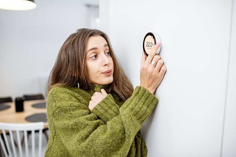 Why Is My Heat Pump Turning On and Off Frequently? A girl adjusting the thermostat.