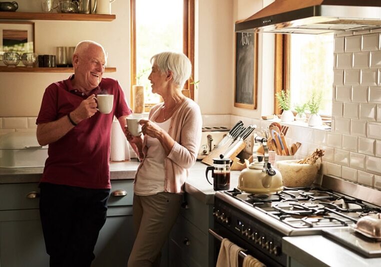 Cold Climate Heat Pumps Are HVAC Game Changers. Photo of an elderly couple enjoying a hot beverage together in their kitchen.